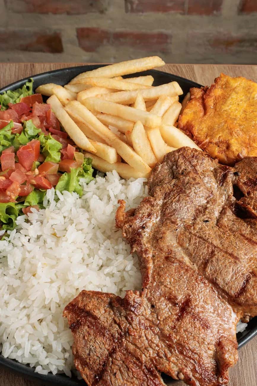 Assiette typique de la cuisine colombienne : viande grillée, riz, patacones et salade